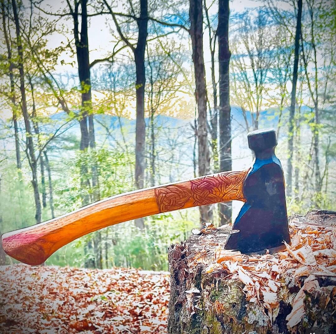 Hand-carved wooden axe handle with intricate Celtic knotwork by A Whittle While, set on a tree stump in the North Georgia woods